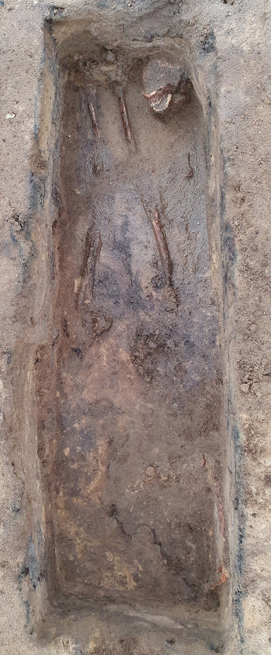 Blick in die geöffnete Grabgrube. Zu erkennen sind der Schädel am Fußende und Beinknochen. (Foto: Daniel Nösler, Lkr. Stade)